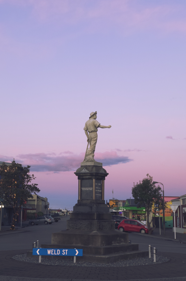 A statue pointing off to the side, with a beautiful pink sky in the background